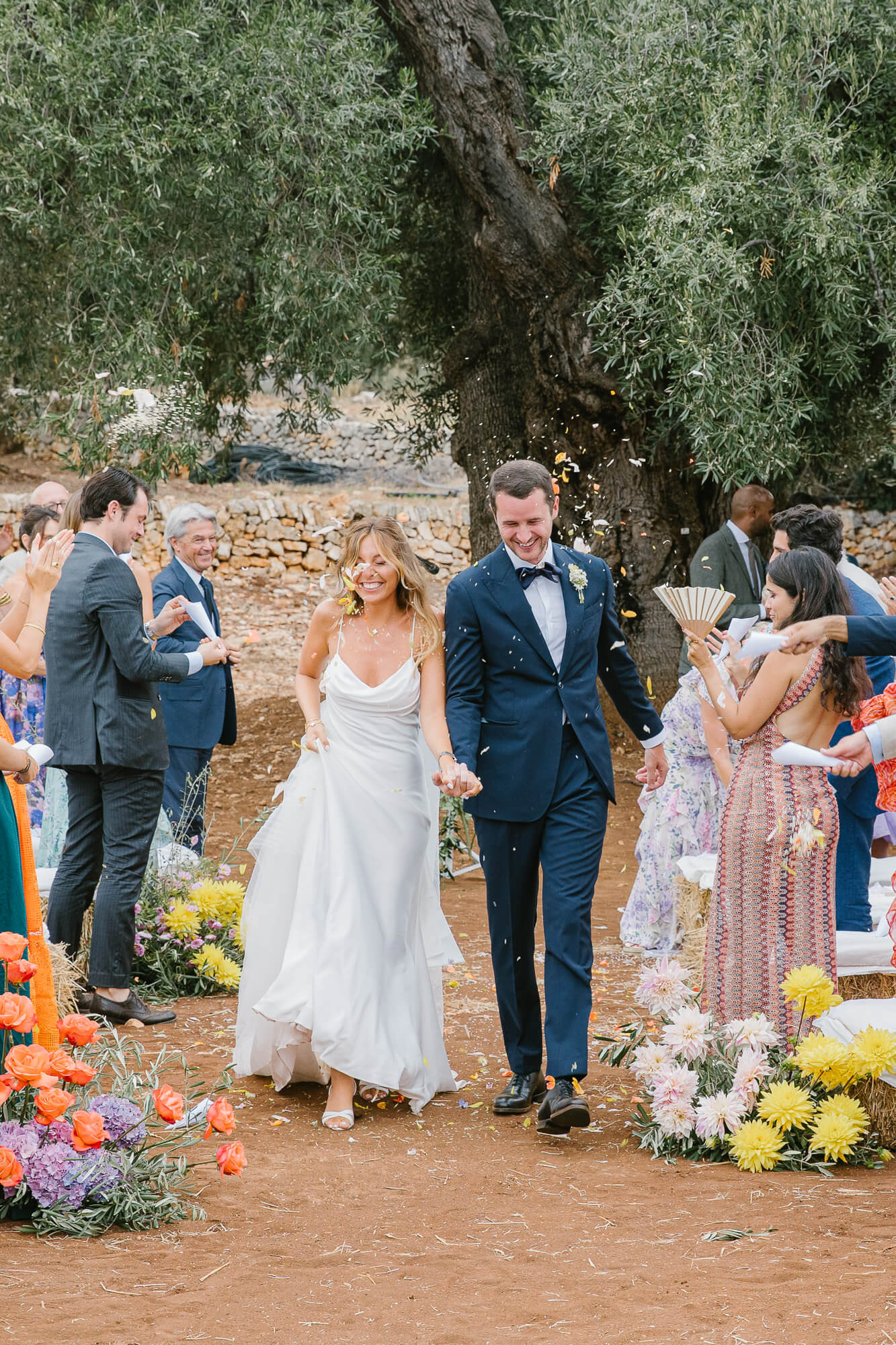 Bride and groom walking down the aisle under a shower of petals in the olive grove
