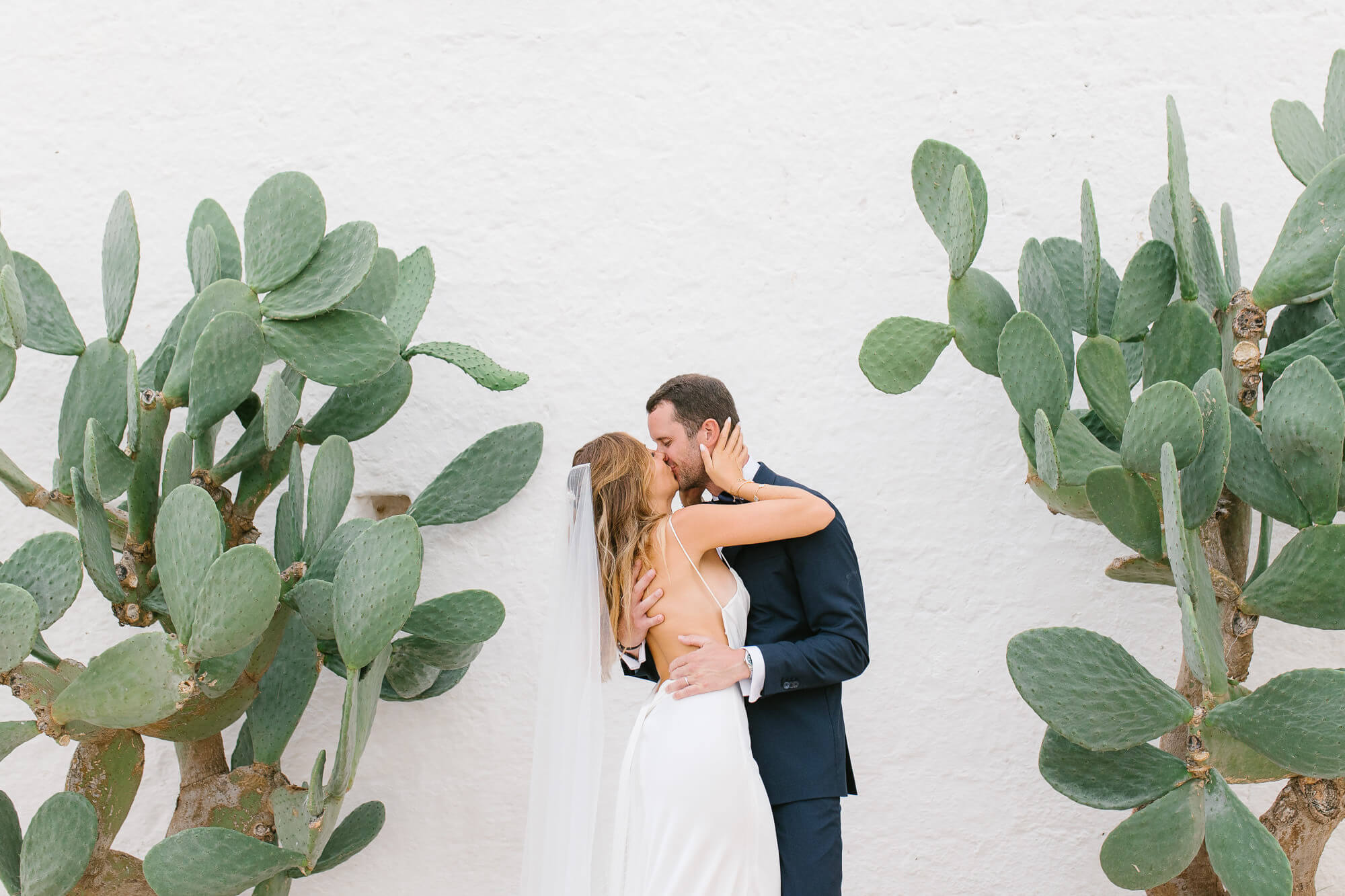 Bride and groom kissing between prickly pears at their Masseria Mozzone wedding in Puglia