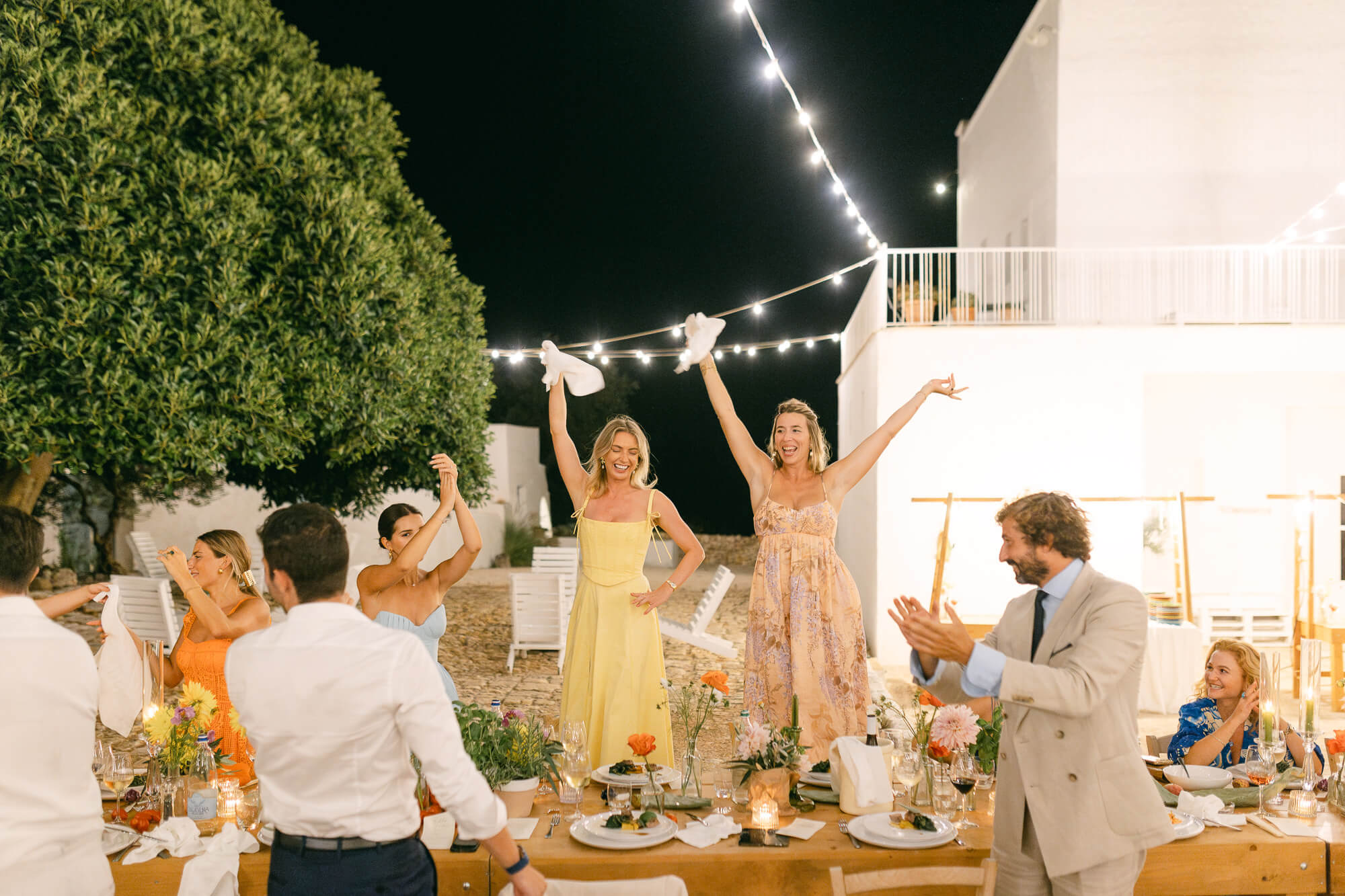 Bridesmaids waving napkins under the string lights