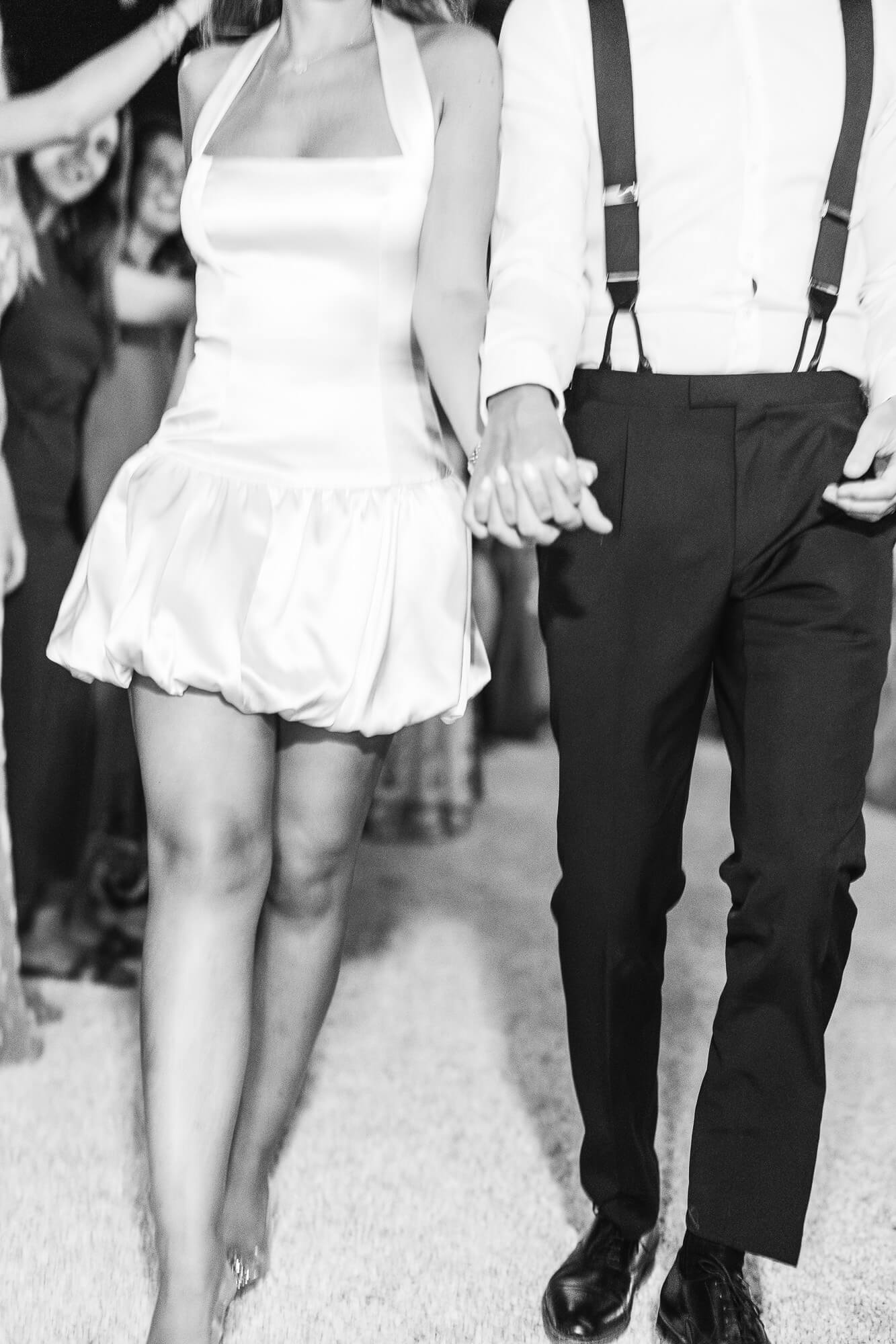 Bride and groom walking hand in hand, black and white detail