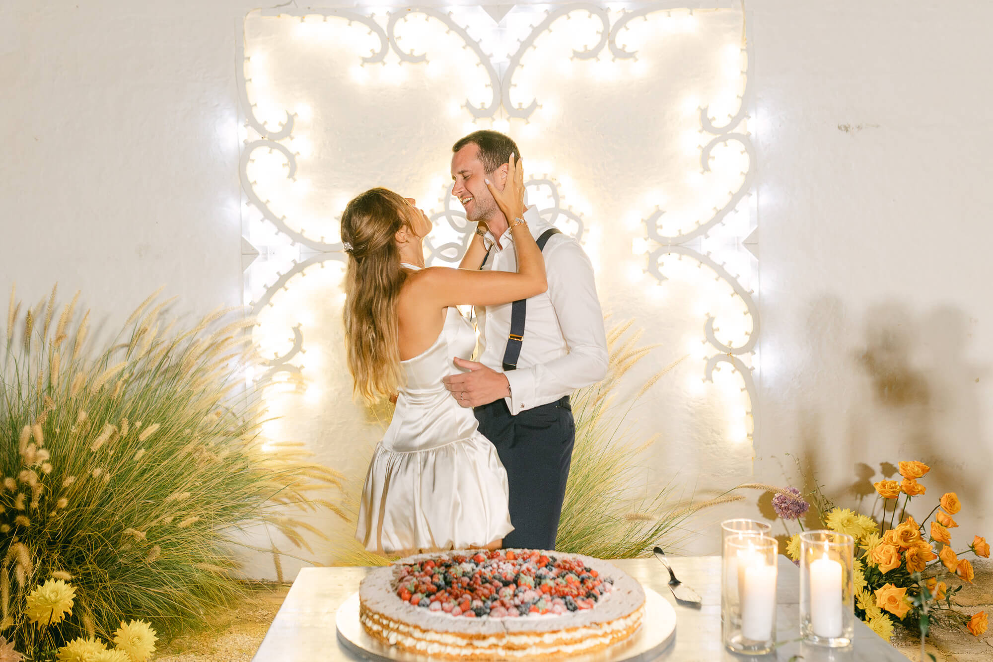 Bride and groom cutting a fruit tart in front of glowing luminarie