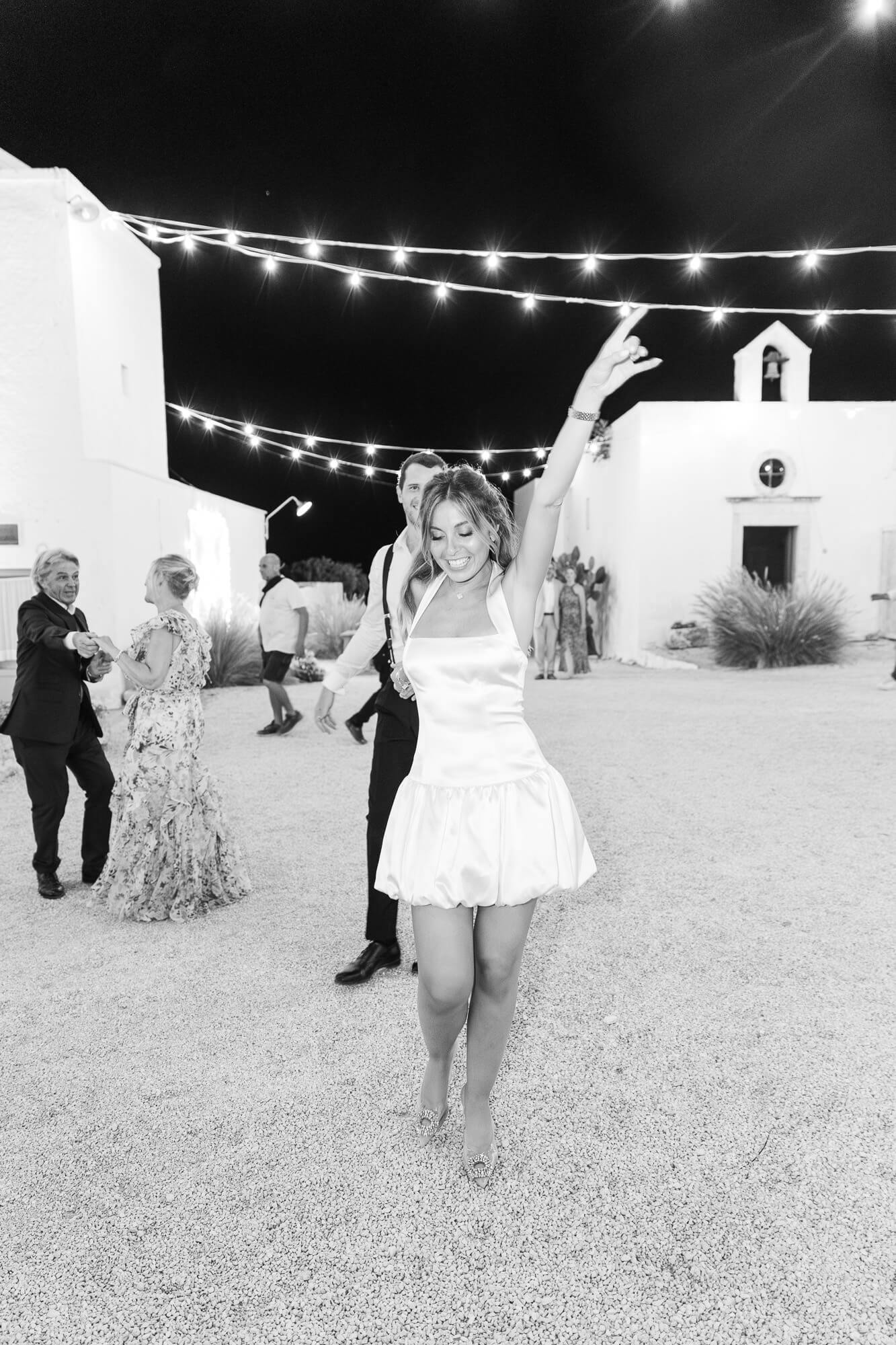 Bride dancing in her short second dress under the string lights